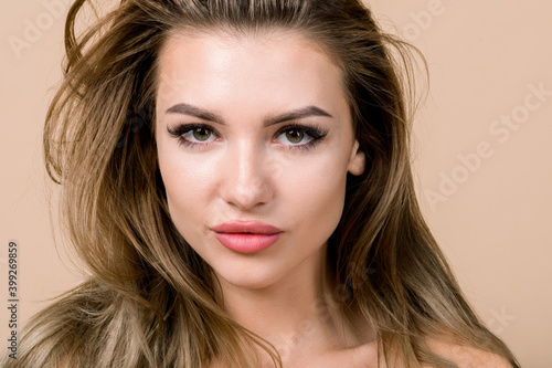 Close up beauty portrait of attractive young stunning European blond woman with natural make up, looking at camera, over beige background with copyspace. Beauty, skin care, cosmetology