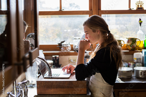 Teenage girl in a kitchen following a baking recipe on a laptop.  photo