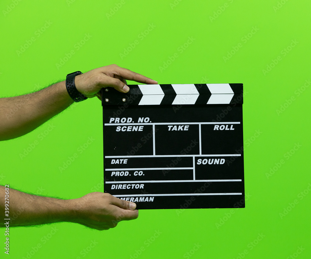 Men's hand holding camera slate for the filming isolated on green background. clapperboard in chroma
