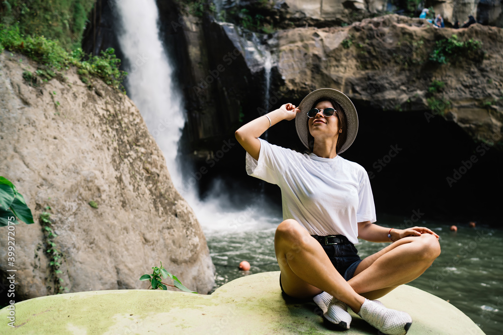 Relaxed female traveler sitting near waterfall