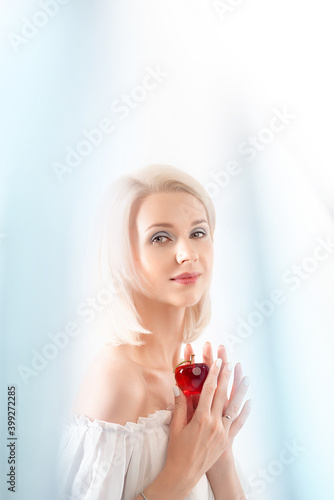a delicate portrait of a beautiful smiling woman with a glass apple in her hands on a white background between blurred blue ribbons