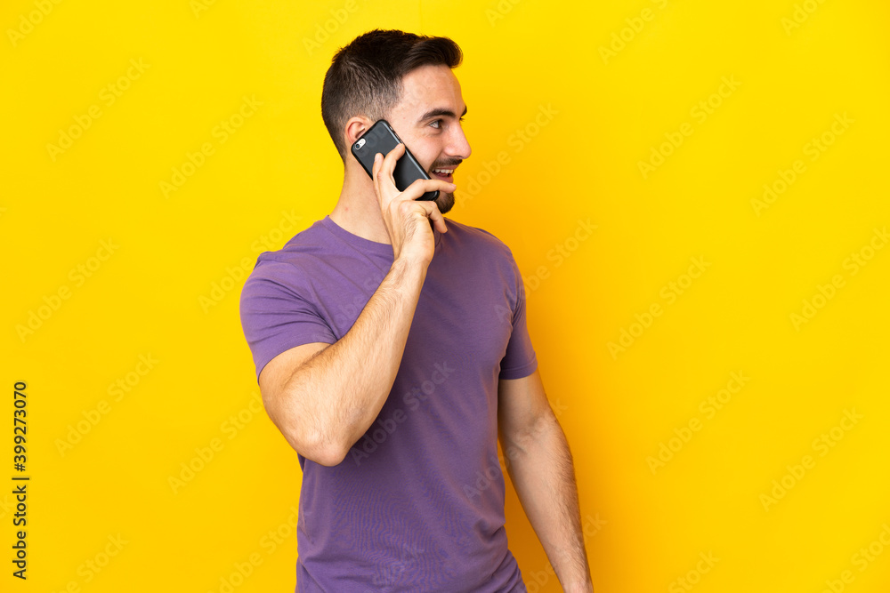 Young caucasian handsome man isolated on yellow background keeping a conversation with the mobile phone with someone Young caucasian handsome man isolated on yellow background keeping a conversation with the mobile phone with someone