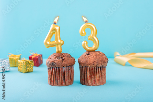 43 Number gold candle on a cupcake against a pastel blue background forty third year celebration