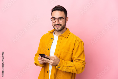 Young caucasian handsome man isolated on pink background sending a message with the mobile photo