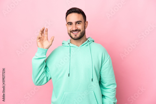 Young caucasian handsome man isolated on pink background saluting with hand with happy expression © luismolinero