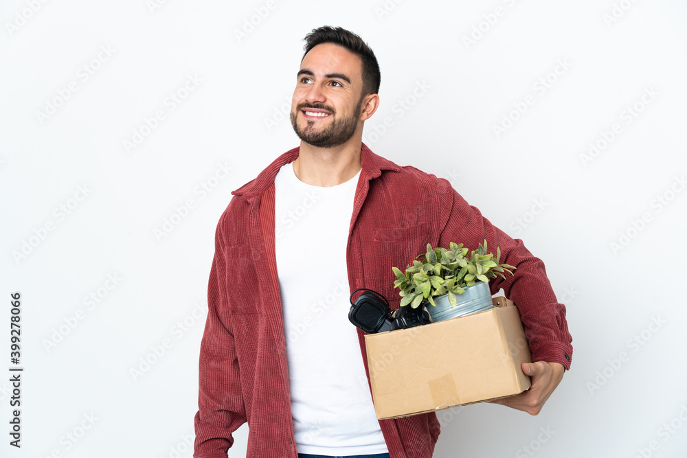 Young caucasian man making a move while picking up a box full of things isolated on white background thinking an idea while looking up Young caucasian man making a move while picking up a box full of things isolated on white background thinking an idea while looking up