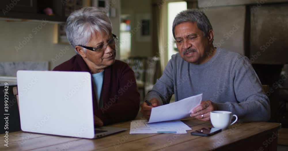 Happy senior mixed race couple doing paaperwork and using laptop Happy senior mixed race couple doing paaperwork and using laptop