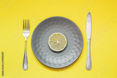 Plate with slice of lemon on yellow background. Diet concept. Colors of the year are Ultimate Gray and Illuminating.