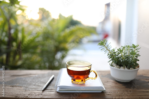Red tea in transparent glass with notebook an plant on drak brown wooden table at outdoor 