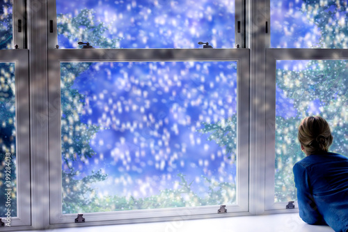 Christmas background with a woman looking at falling snow outside the window. © iweta0077