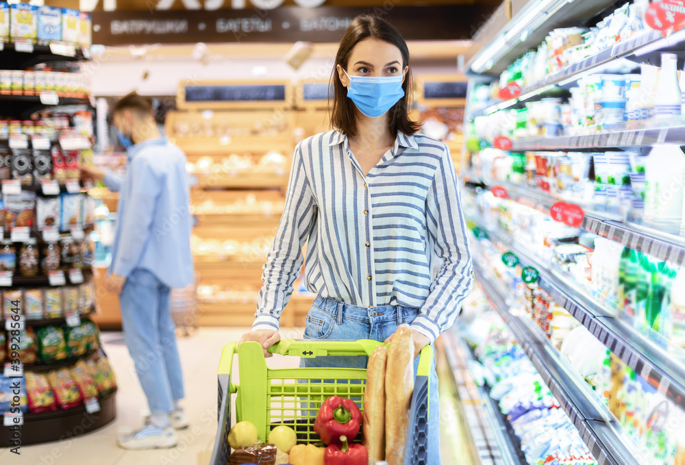 Young woman in face mask shopping in supermarket with cart