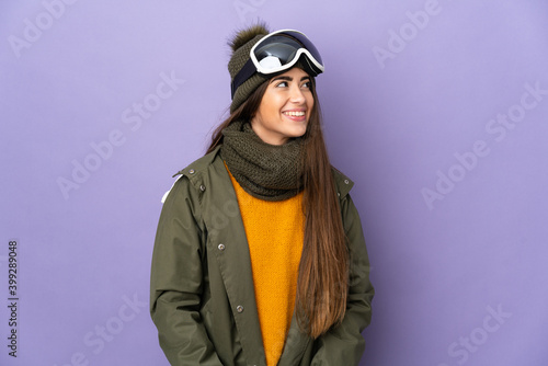 Skier caucasian girl with snowboarding glasses isolated on purple background thinking an idea while looking up