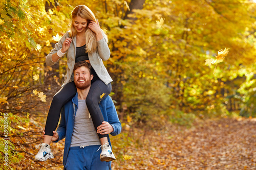woman sits on male's neck during walk, happy couple relax and have fun in the autumn nature, wearing casual sportive clothes, on fresh air outdoors