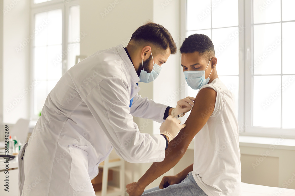 Doctor in face mask giving antiviral vaccine to young patient during vaccination campaign Doctor in face mask giving antiviral vaccine to young patient during vaccination campaign