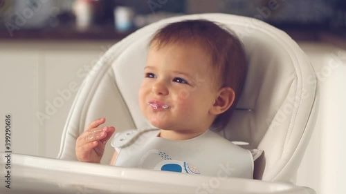 baby daughter on high chair in home kitchen takes a spoon with baby food from mother's hand