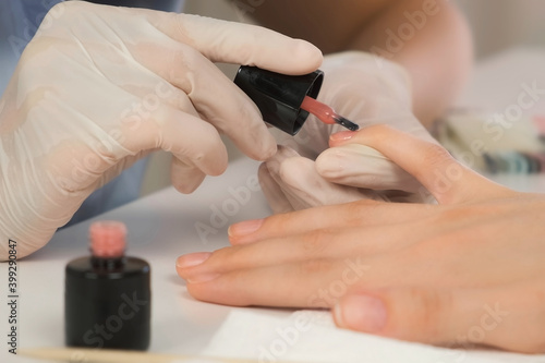 Woman manicurist master is applying pink gel on client s nails in beauty salon  hands closeup. Manicure nail paint. Nail polish. Hygiene care about nails. Beauty procedure.