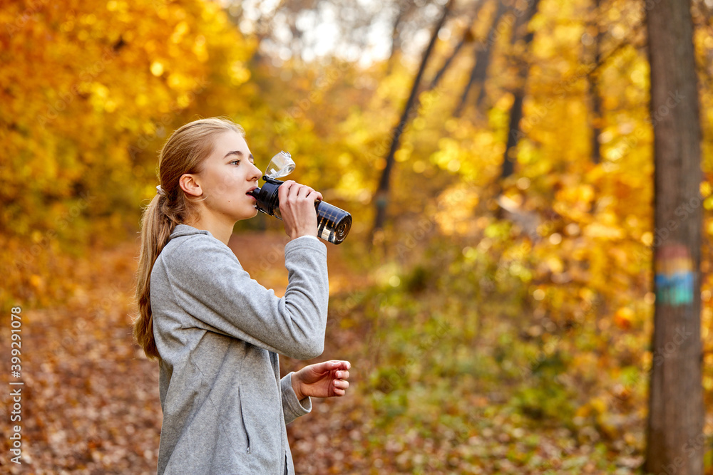 woman drinking water from a bottle, caucasian female refresh her body after running workout at sunny autumn day. running makes your body stronger