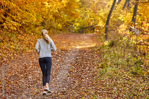 female running jogging in the forest, wearing sport clothes, at sunny autumn weather. sport, workout, run, wellbeing concept. rear view
