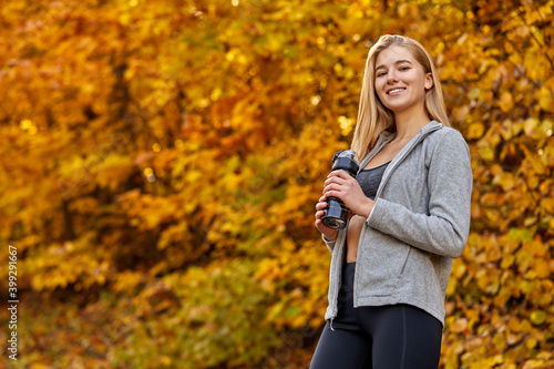 runner with bottle of water standing in autumn forest nature  take a break  contemplating nature around. sport concept