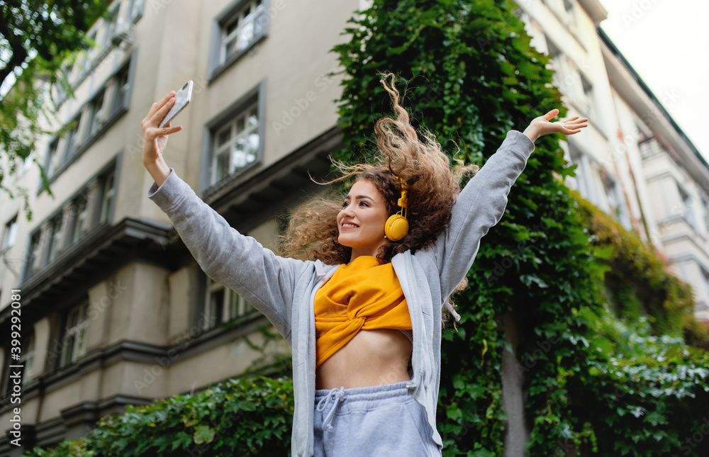 Young woman with smartphone dancing outdoors on street, tik tok concept. - obrazy, fototapety, plakaty 