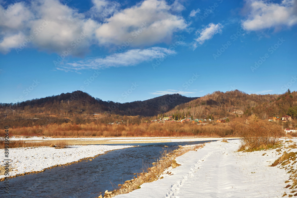 Calm winter mountain river, on a clear sunny day, against the background of mountains and blue sky with white clouds