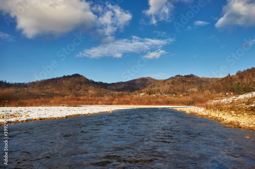 Calm winter mountain river, on a clear sunny day, against the background of mountains and blue sky with white clouds