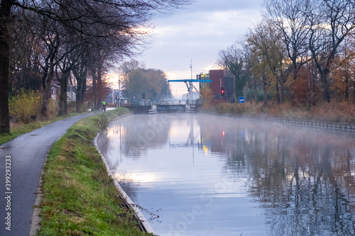 River stream canal bending with grass banks and wild flowers and trees in a scenic landscape on a misty autumns morning sunrise day. High quality photo