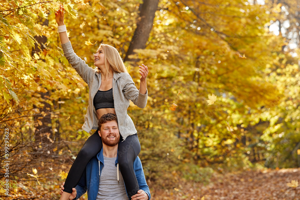 woman sits on male's neck during walk, happy couple relax and have fun in the autumn nature, wearing casual sportive clothes, on fresh air outdoors woman sits on male's neck during walk, happy couple relax and have fun in the autumn nature, wearing casual sportive clothes, on fresh air outdoors