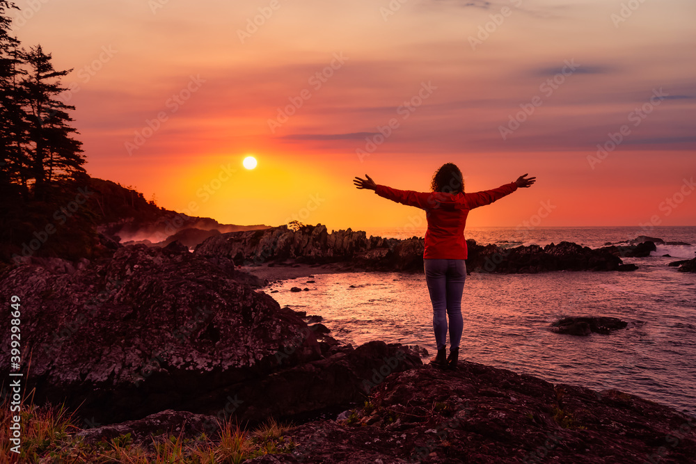 Fototapeta premium Wild Pacifc Trail, Ucluelet, Vancouver Island, BC, Canada. Adventurous Girl Enjoying the Beautiful View of the Rocky Ocean Coast. Colorful Sunset Sky. Concept: Travel, adventure, freedom