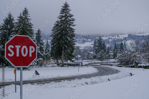 stop road sign across winter landscape in snow and road going to the mountains. Mountains villgae in snow. Pine trees, forest and houses © Kate