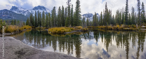 Snow capped Mount Lawrence Grassi mountain with blue sky and white clouds reflect on water surface in autumn. Beautiful natural scenery landscape at Canmore, Canadian Rockies, Alberta, Canada.