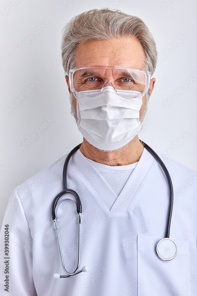confident male doctor in mask, mature elderly male looks at camera wearing white medical suit and goggles, using stethoscope, white background confident male doctor in mask, mature elderly male looks at camera wearing white medical suit and goggles, using stethoscope, white background