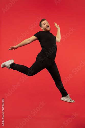 Inspired. Full length portrait of young successfull high jumping man gesturing isolated on red studio background. Attractive male caucasian model. Copyspace. Human emotions, facial expression concept. © master1305
