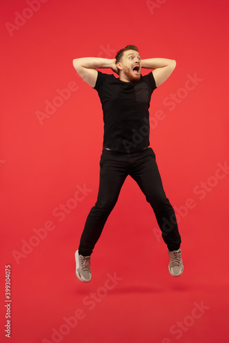 Winner. Full length portrait of young successfull high jumping man gesturing isolated on red studio background. Attractive male caucasian model. Copyspace. Human emotions, facial expression concept. © master1305
