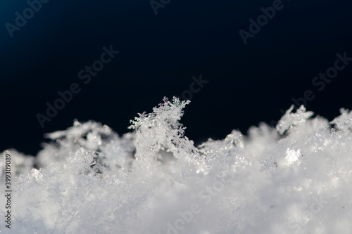 Snowflakes on a blurry background of white snow and dark blue background. Abstract white and blue natural winter background