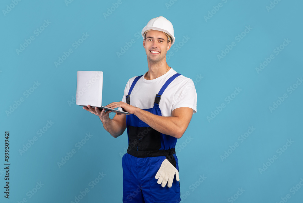 Man in coveralls and hard hat using laptop computer on blue background Man in coveralls and hard hat using laptop computer on blue background