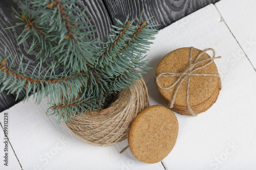 Gingerbread cookies tied with twine. Nearby there is a spruce branch and a skein of twine. On boards painted white.