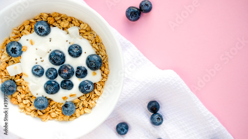 Delicious homemade muesli and blueberries served on a pink table with a white napkin, top view with space for text. Healthy breakfast