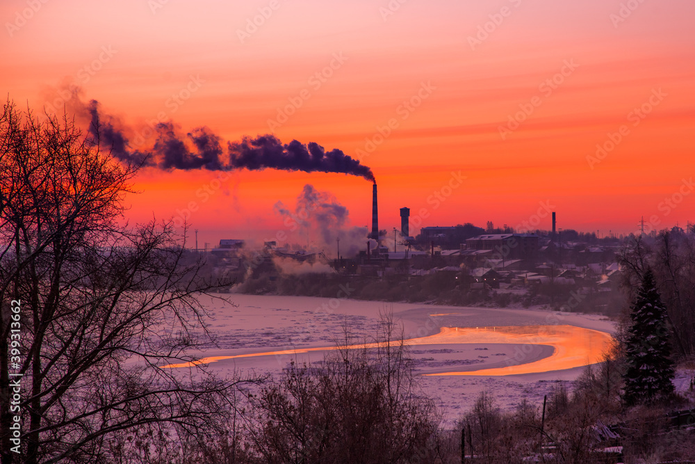 the first rays of the rising sun paint the clear sky in beautiful colors over the industrial city on the river bank