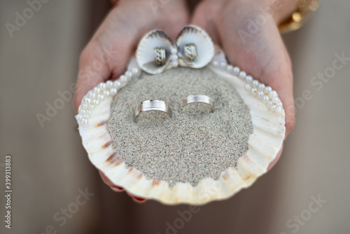 wedding rings inside a shell with sand held by one hand
