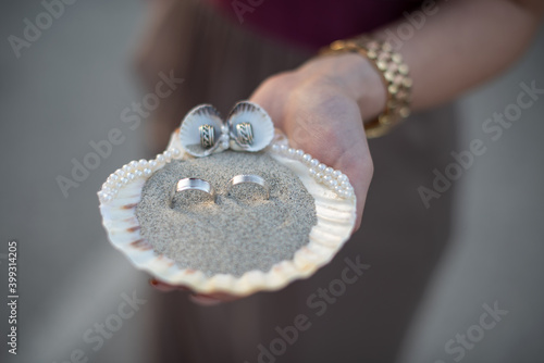wedding rings inside a shell with sand held by one hand