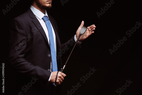 Fototapeta Male dominant businessman in a suit holding a leather whip Flogger for dominatio