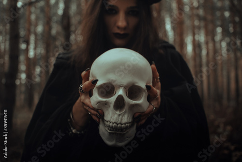 frightening evil witch in black rags holds a dead man's skull in her hands for a dark ritual
