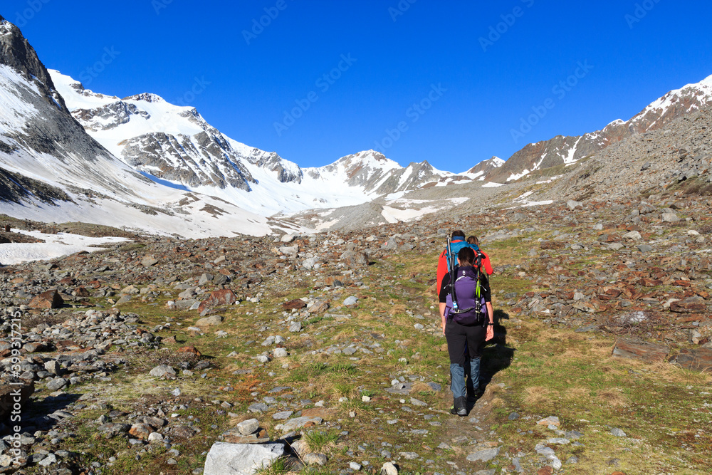 Group of people hiking towards glacier Sexegertenferner and mountain snow panorama with blue sky in Tyrol Alps, Austria