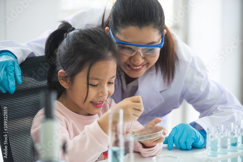Wallpaper Mural little asian children girl in elementary science class doing chemical experiment helped by woman teacher test, experimen, try drop color water to plate. Education science workshop concept. Torontodigital.ca