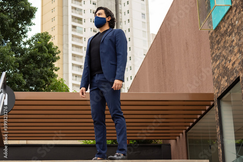Homem em paisagem urbana, usando blazer e máscara de proteção contra covid-19.