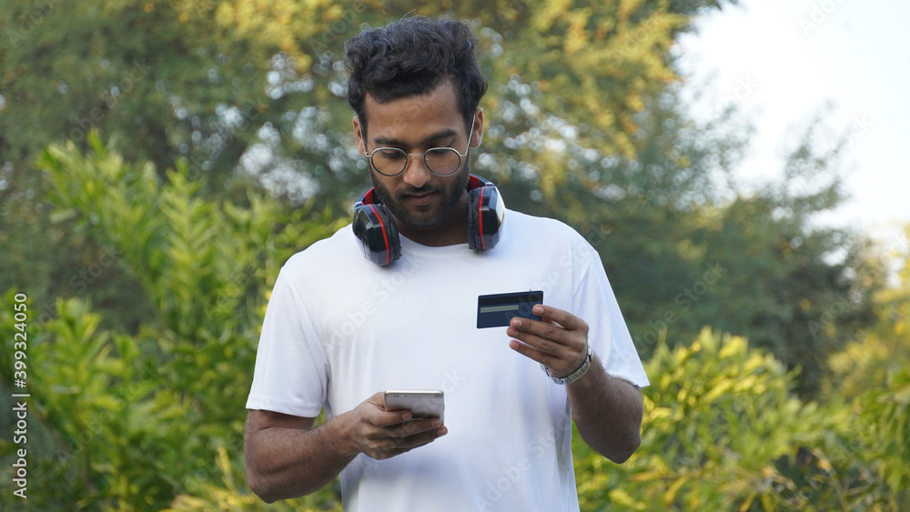 Cheerful young Man guy in casual shirt, White t-shirt posing isolated on Beautiful background. People lifestyle concept. Using mobile phone hold credit bank card Cheerful young Man guy in casual shirt, White t-shirt posing isolated on Beautiful background. People lifestyle concept. Using mobile phone hold credit bank card