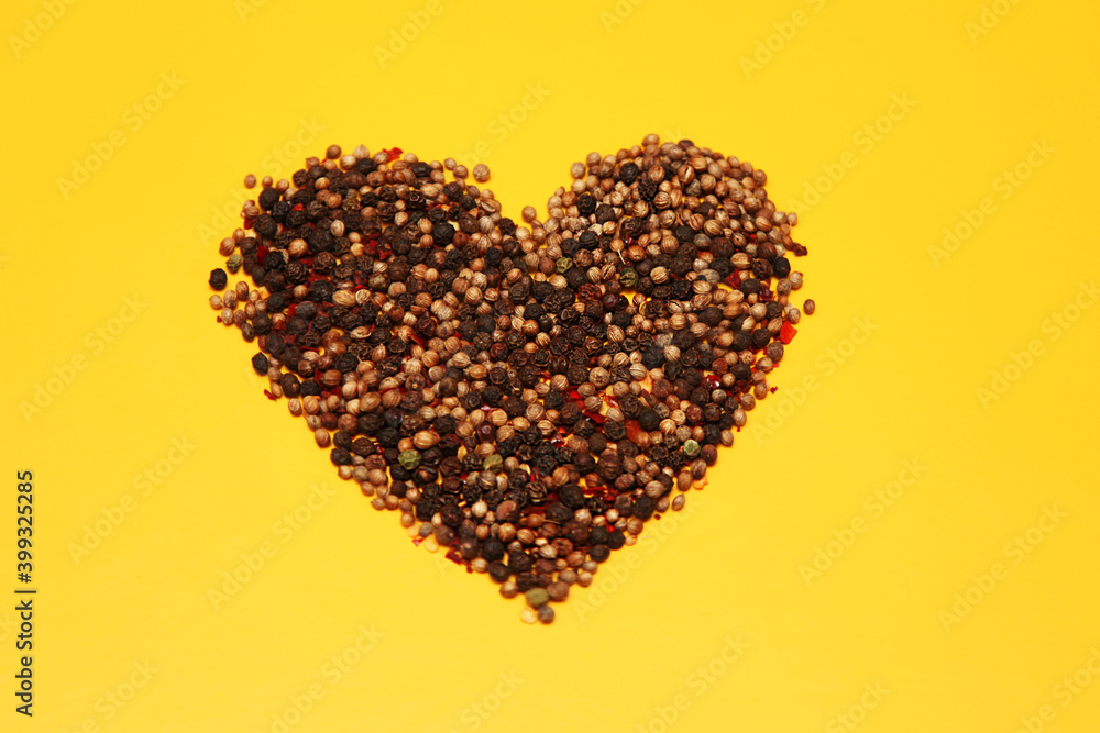 A mixture of peppers-allspice, black, red, green, white-in the shape of a heart on a yellow background in the center