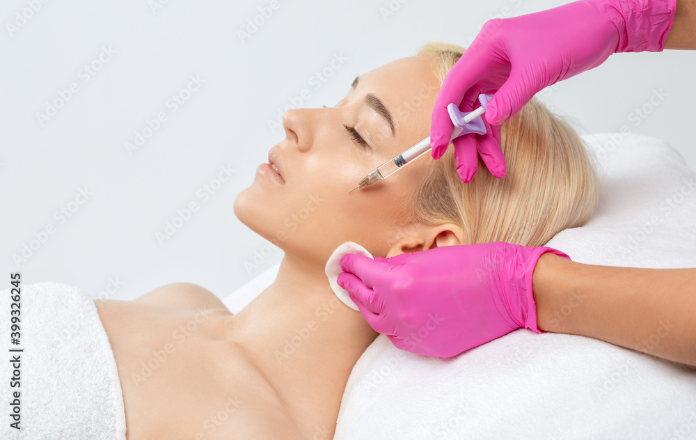 Fototapeta premium Cosmetologist makes rejuvenating anti wrinkle injections on the face of a beautiful blonde woman. Female aesthetic cosmetology in a beauty salon.