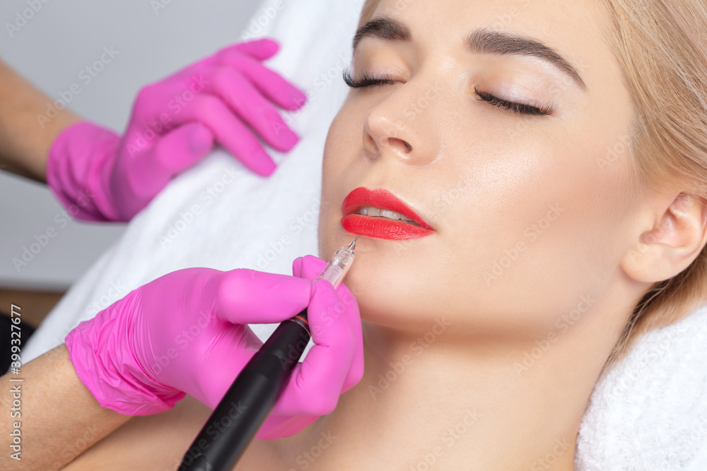 Permanent make-up for red Lips of beautiful blonde woman in beauty salon. Closeup beautician doing  tattooing Lips. Female aesthetic cosmetology in a beauty salon.